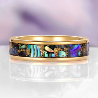 Gold ring with colorful gemstone inlay on a reflective surface with a blurred background