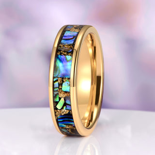 Gold ring with colorful inlay on a white surface with a blurred purple background