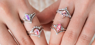 Four silver engagement rings with pink center stones on hands over a light background 