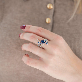 Silver leaf guard wedding band with blue sapphire and diamond accents and oval sparkly blue sandstone engagement ring displayed in hand against warm brown backdrop