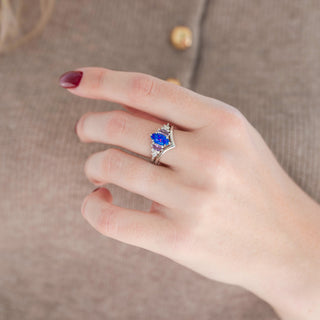 Silver marquise purple and pink opal engagement ring set with marquise pink sapphire and diamond accents paired with a chevron band displayed in hand against a warm brown background