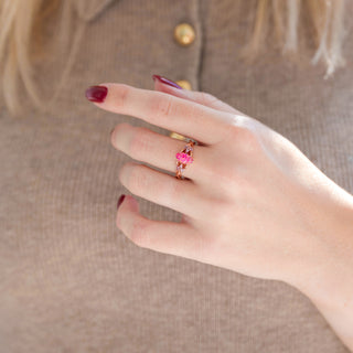 Rose gold Celtic pink opal engagement ring with pink sapphire accent stones displayed in hand against warm brown backdrop