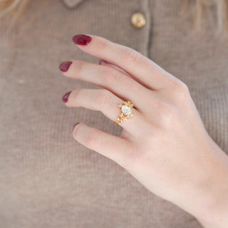 Yellow gold leaf engagement ring with oval-shaped diamond displayed in hand against warm brown backdrop