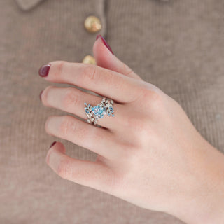 Sterling silver leaf guard wedding band and pear-shaped aquamarine engagement ring displayed in hand against warm brown backdrop