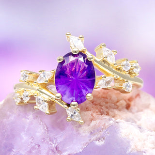 Gold ring with a purple gemstone on a pink and purple gradient background