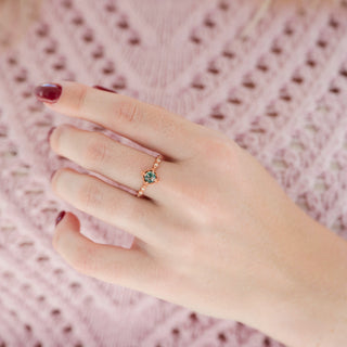 Rose gold round-cut green moss agate engagement ring with diamond accents displayed in hand against a warm pink background