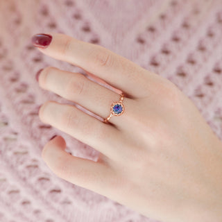 Rose gold round-shaped alexandrite engagement ring with scalloped design displayed in hand against warm pink backdrop