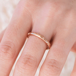 Rose gold 2mm wedding band with floral design on hand over a light background 