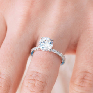 White gold engagement ring with round cut diamond center stone and accents on hand over light background
