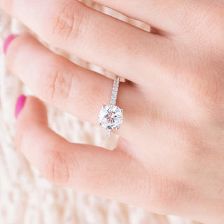 White gold engagement ring with round cut diamond center stone and accents on hand over light background