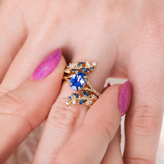 Yellow gold ring with leaf design and blue sapphire center stone on hand over light background