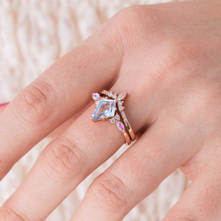 Rose gold ring set with kite cut natural aquamarine center stone and moonstone accents on hand over a light background 
