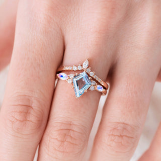 Rose gold ring set with kite cut natural aquamarine center stone and moonstone accents on hand over a light background 