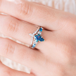 White gold engagement ring set with kite cut blue fire opal center stone and London blue topaz and diamond accents on hand over a light background 