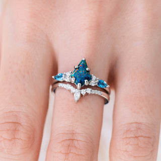White gold engagement ring set with kite cut blue fire opal center stone and London blue topaz and diamond accents on hand over a light background 