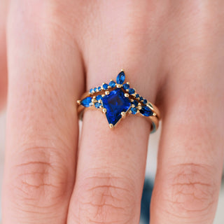 Yellow gold engagement ring set with kite cut lab-grown blue sapphire center stone and accents on hand over a light background 