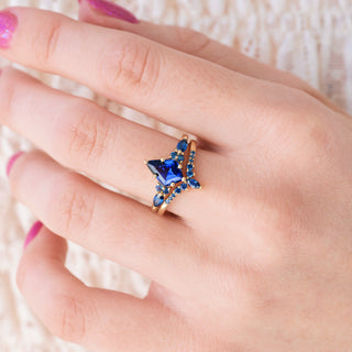 Yellow gold engagement ring set with kite cut lab-grown blue sapphire center stone and accents on hand over a light background 