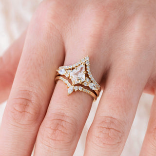 Yellow gold engagement ring set with kite cut diamond center stone and accents on hand over a light background 