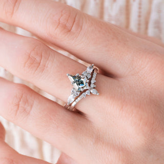 White gold engagement ring set with kite cut gray moissanite center stone and diamond accents on hand over light background