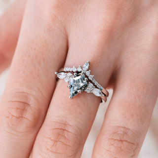 White gold engagement ring set with kite cut gray moissanite center stone and diamond accents on hand over light background