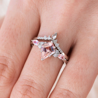White gold engagement ring set with kite cut natural peachy pink morganite center stone and diamond accents on hand over light background