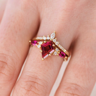 Yellow gold engagement ring set with kite cut ruby center stone and diamond accents on hand over a light background 