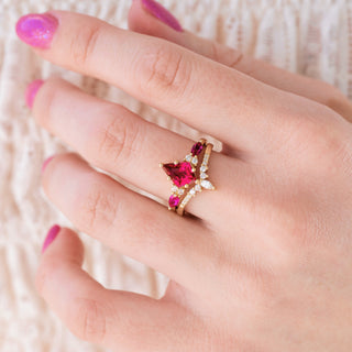 Yellow gold engagement ring set with kite cut ruby center stone and diamond accents on hand over a light background 