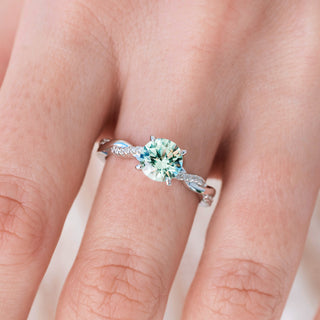 Twisted silver ring with round cut green sapphire center stone and diamond accents on hand over a light background 