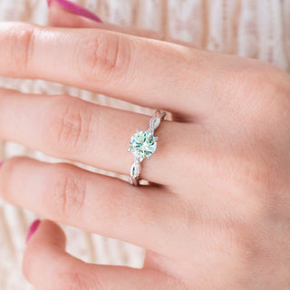 Twisted silver ring with round cut green sapphire center stone and diamond accents on hand over a light background 