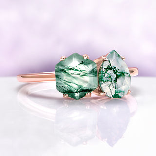 Pair of green gemstone earrings on a reflective surface with a light purple background