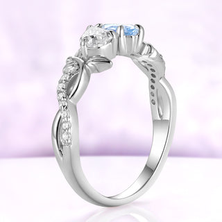 Side profile of the simulated aquamarine toi et moi ring in sterling silver, the two strands of the vine band crossing below the setting