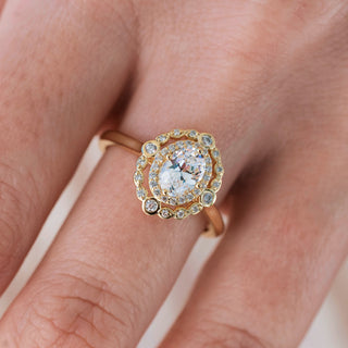 Yellow gold engagement ring with oval cut diamond center stone and diamond accents on hand over a light background 