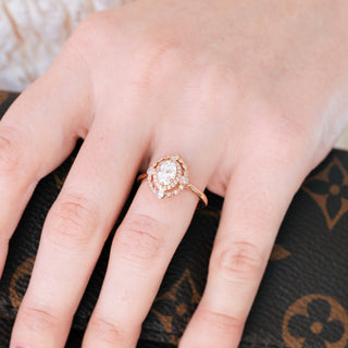 Rose gold engagement ring with oval cut diamond center stone and accents on hand over a dark background 