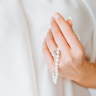 Hand holding a pearl necklace with a diamond ring on a light background