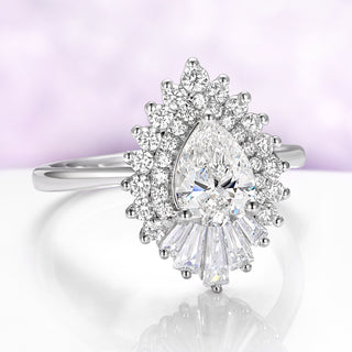 Diamond ring with a pear-shaped center stone on a reflective surface with a light purple background