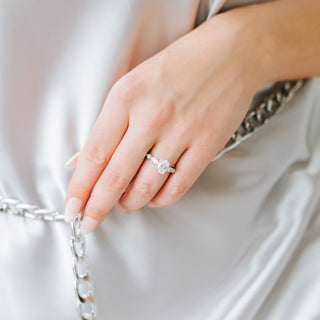 Oval cut diamond ring on a hand against a neutral background with a chain 