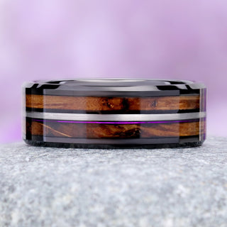 Front view of the black tungsten band on granite showing the whiskey barrel oak grain and the purple fishing line along the silver rail