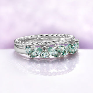 Silver ring with green gemstones on a light purple background