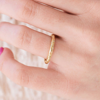 Yellow gold 2mm wedding band with floral design on hand over a light background 