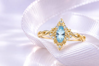 Gold marquise aquamarine ring with a braided band resting on white satin ribbon