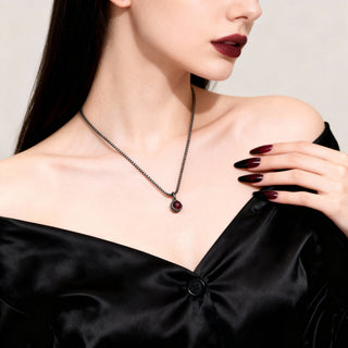 Woman wearing a black necklace with a red gemstone against a neutral background
