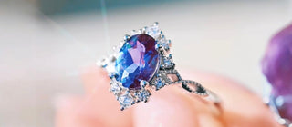 Close-up of a ring with a purple gemstone held by a hand against a blurred background