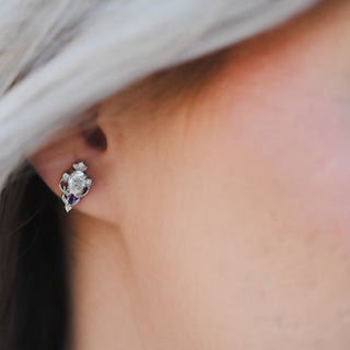 Close-up of the Carmilla moissanite and amethyst stud earring worn on the ear, showing scale