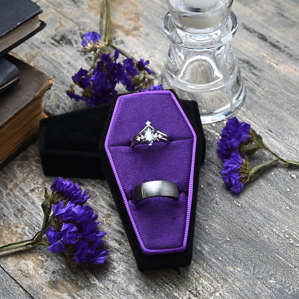 Black and purple coffin double ring box on weathered wood with old books and purple flowers