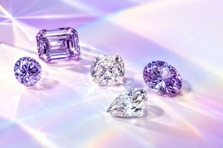 Loose lilac and lavender gemstones in round, emerald, cushion, oval and pear cuts on a pale lilac surface with rainbow prism light, Aquamarise Compassion page mobile banner