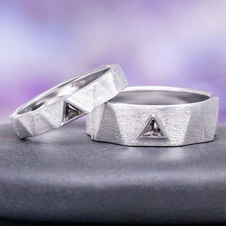 Two silver rings with geometric designs on a gray surface with a purple gradient background