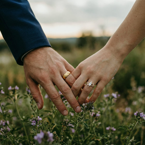 Two hands holding each other in a field of flowers with a blurred natural background