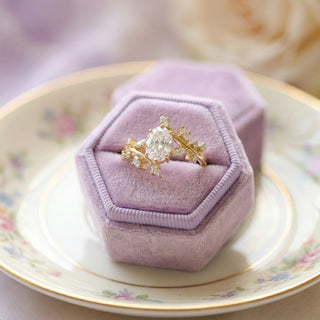 Gold ring with a large diamond in a purple velvet box on a floral plate