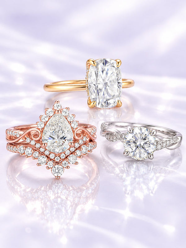 Three engagement rings on lilac satin: elongated cushion solitaire in yellow gold, pear halo bridal set in rose gold and round solitaire with twisted band in white gold, Aquamarise banner