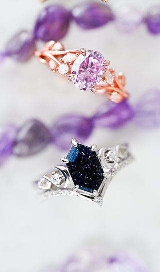 Close-up of a silver ring with a blue gemstone and a pink gemstone ring on a blurred purple background.